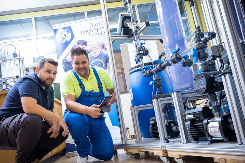Zwei Schüler in Arbeitskleidung stehen neben einem Wasserkasten im Labor