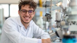 Junger lächelnder Schüler in Kittel sitzt neben Maschinen