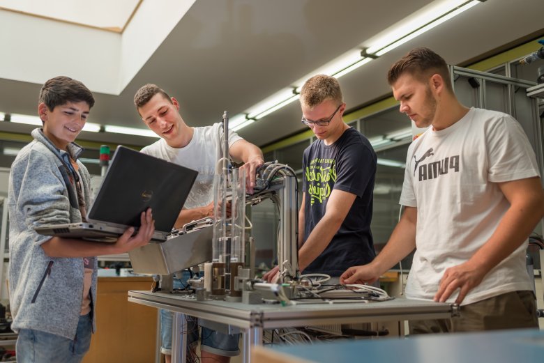 Vier Schüler arbeiten an einem Projekt mit vielen Kabeln, einer der Schüler hält einen Laptop in der Hand
