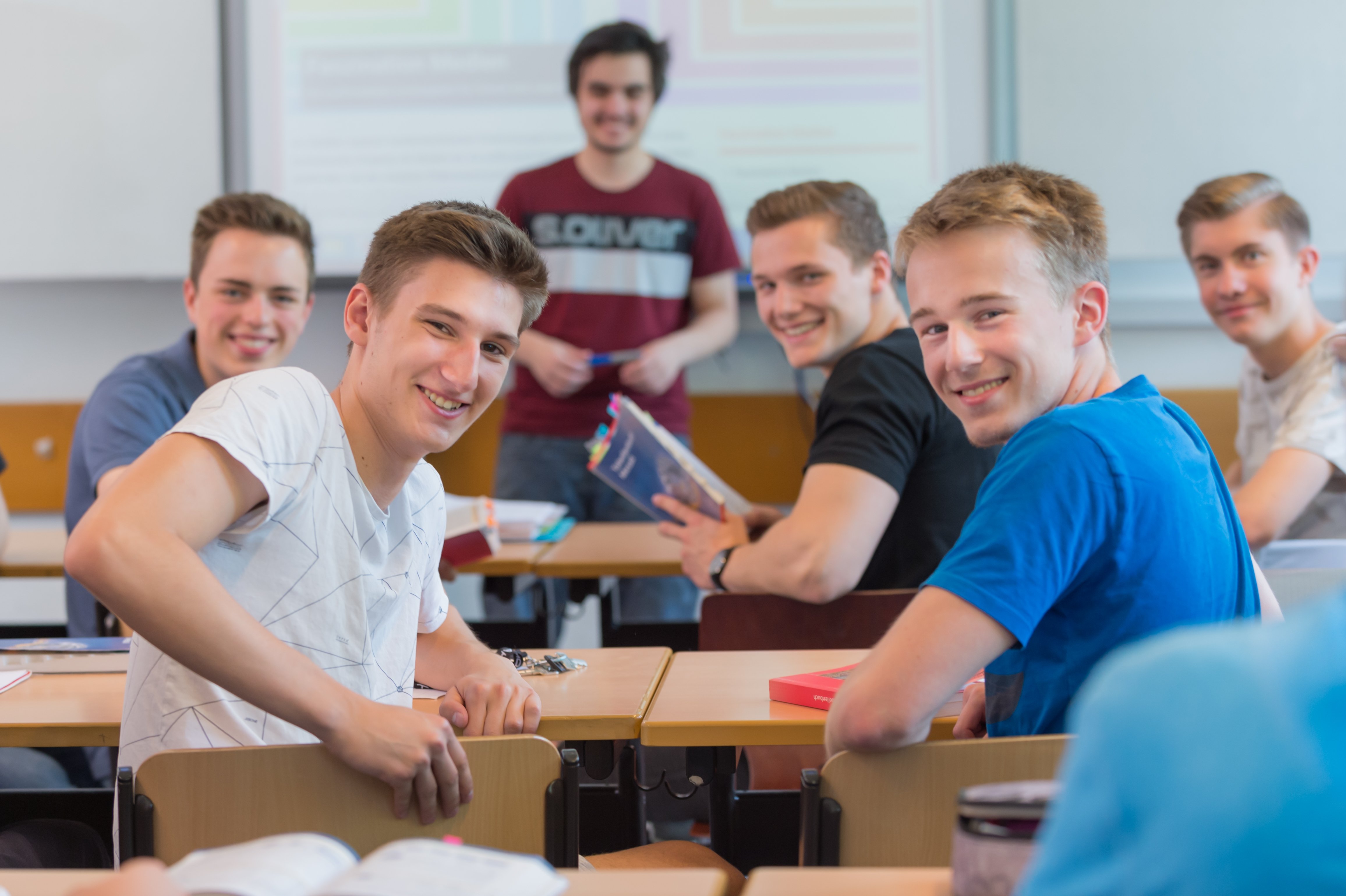 Gutgelaunte Schüler blicken einen an. Sie sitzen in einer Klasse. 