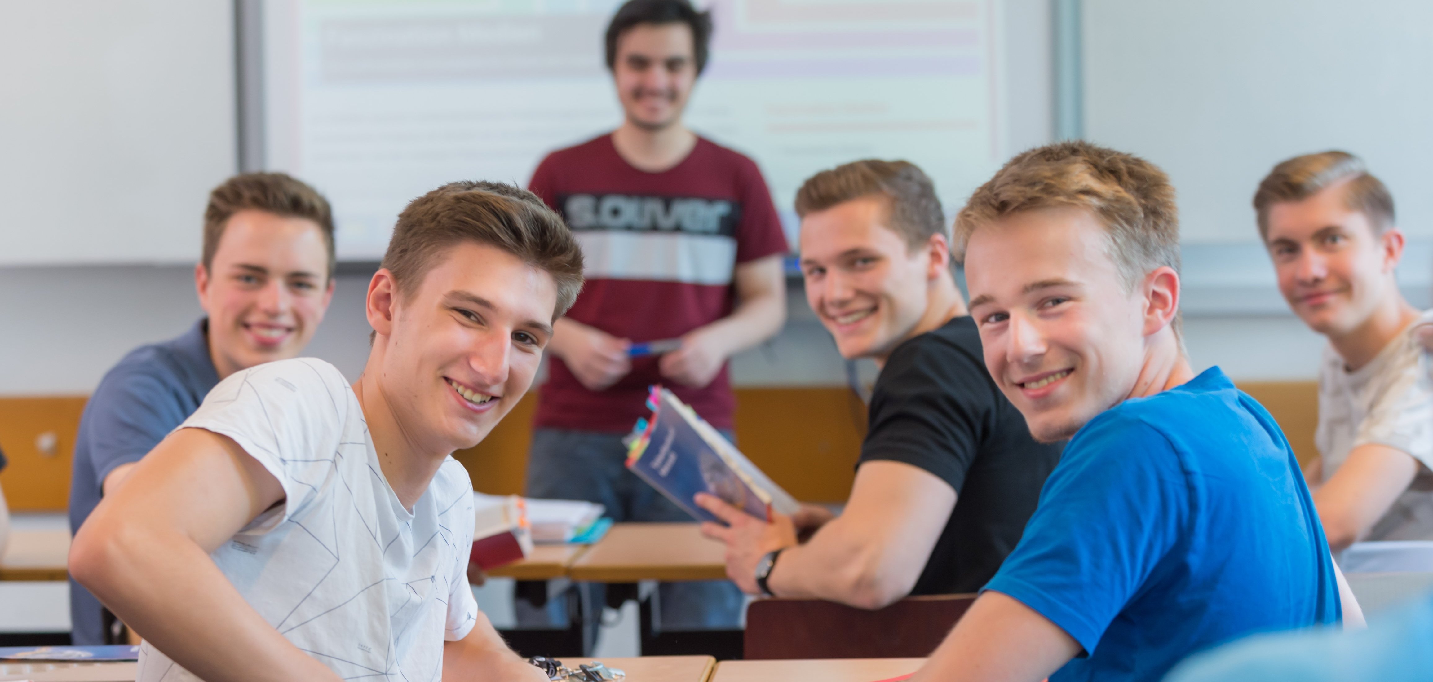 Gutgelaunte Schüler blicken einen an. Sie sitzen in einer Klasse.