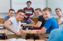 Gutgelaunte Schüler blicken einen an. Sie sitzen in einer Klasse. 