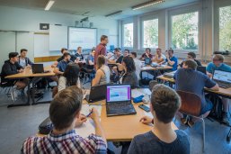 Lehrer steht in der Mitte des Klassenraumes zwischen allen Schülern