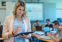 Motivierte junge Lehrerin hält Stift und dazugehöriges Tablet in der Hand und schaut auf ihr Tablet