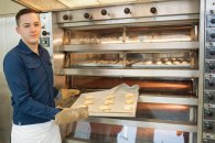 Ein Schüler steht vor einem großen Ofen und präsentiert ein Blech mit Keksen.