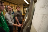 Ein Lehrer und zwei Schüler kontrollieren die Programmierung einer CNC-Fräse.