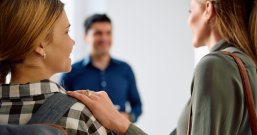 Das Bild zeigt einen Lehrer in Gespräch mit einer Mutter und ihrer Tochter, die Schülerin ist.