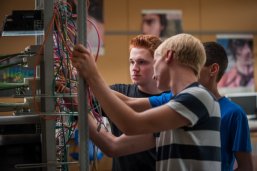 Drei Schüler arbeiten an einem Netzwerkschrank.