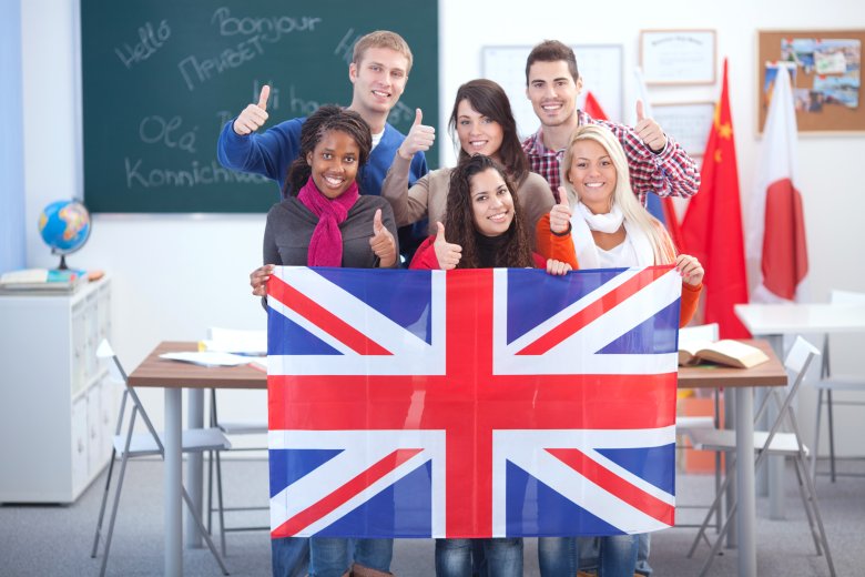 Language school. eine Gruppe von Schülern stehen im Klassenraum und halten die Flagge von Großbritannien hoch.