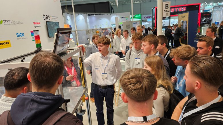 Momentaufnahme einer Messe mit Zuschauern und einem Schüler, der die mitgebrachte Gerätschaft erklärt