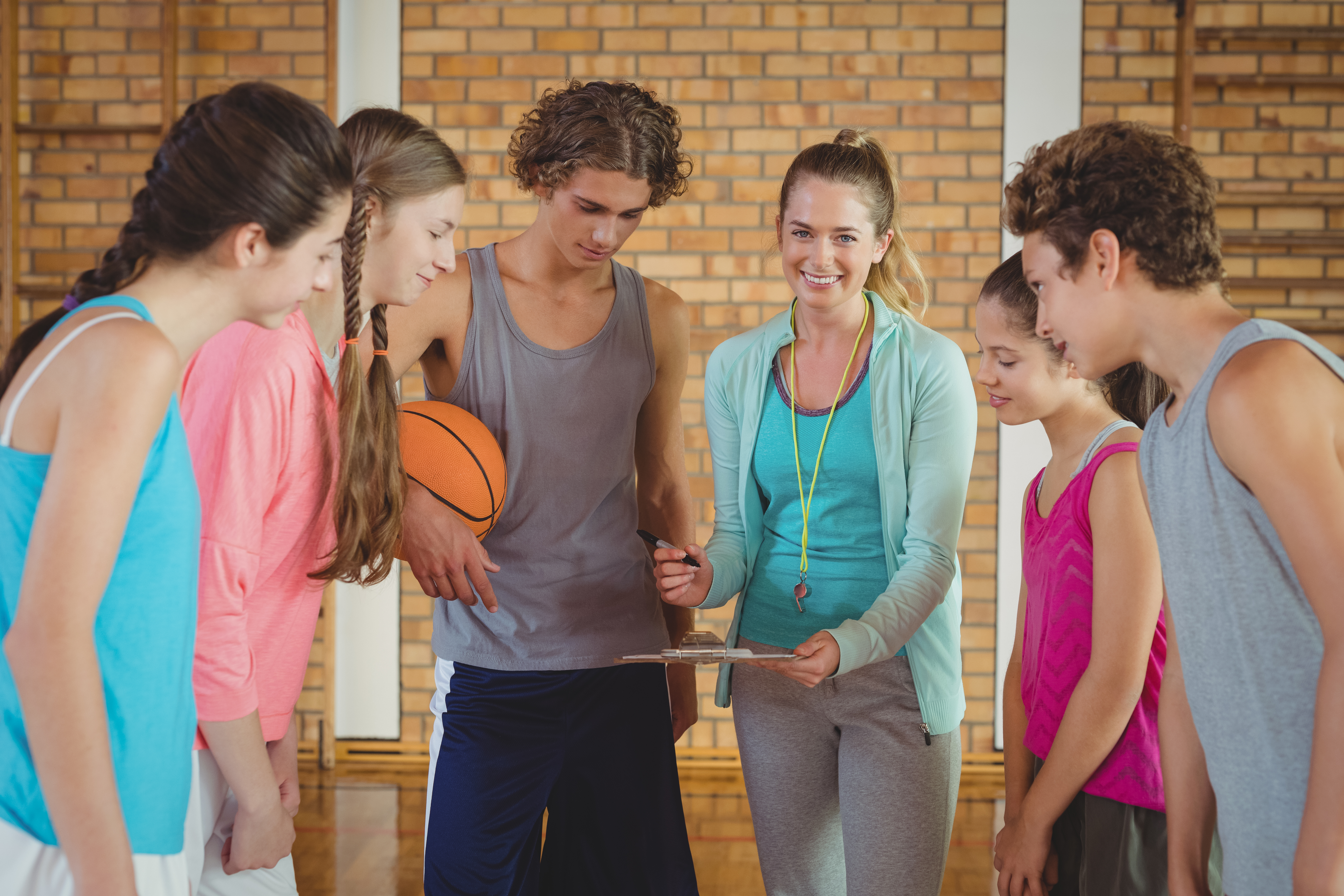 Portrait of female coach mentoring high school kids in basketball court